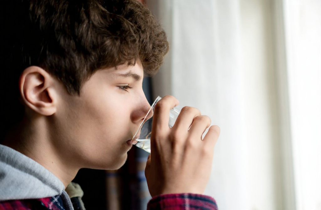A teen drinks cool water to hydrate their nervous system after a root canal.