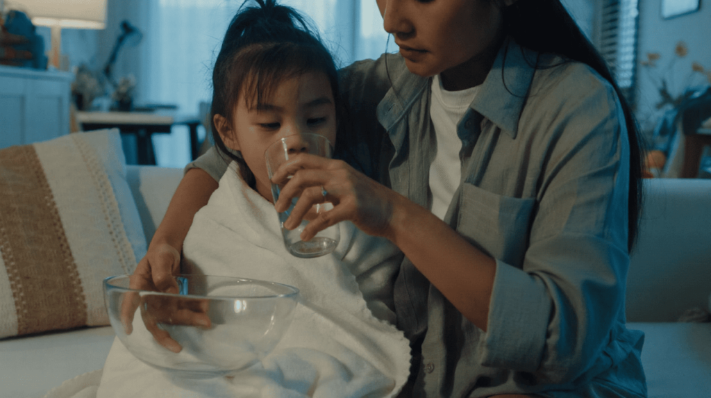 A mother helps her daughter rinse her mouth with lukewarm water to relieve discomfort from a chipped baby tooth.