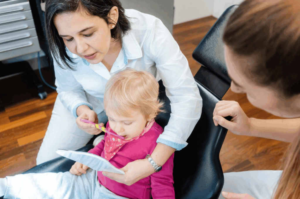 A dentist is teaching a baby how to brush her teeth.